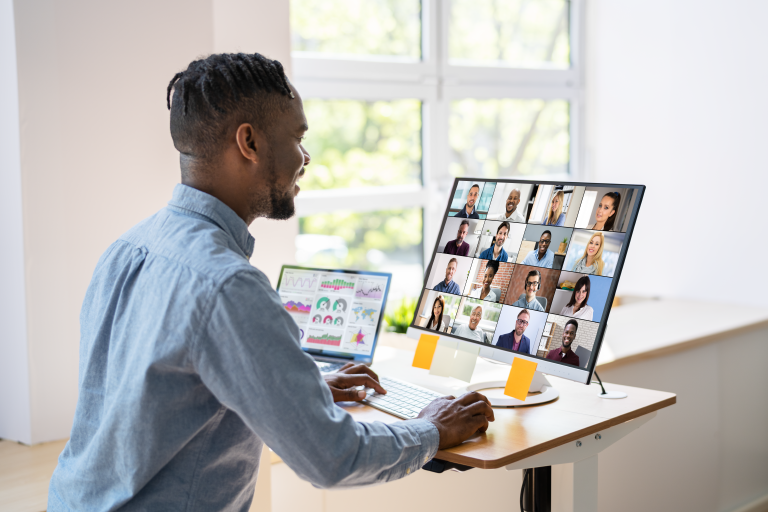 Man sitting at a desk with a computer that is showing a zoom call with several people attending